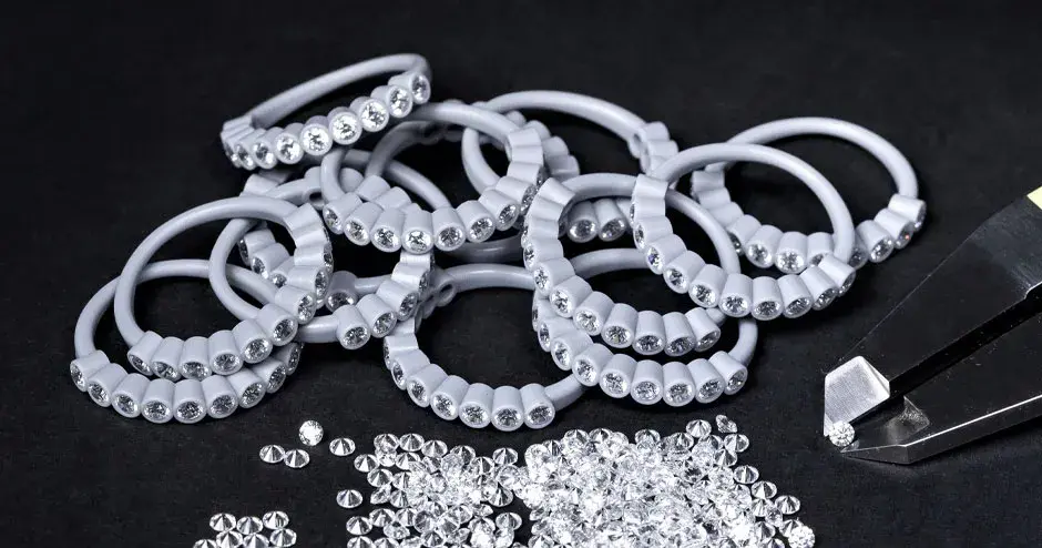 许多镶有钻石的蜡质模型戒指，持有钻石的卡钳尖端，分散的钻石